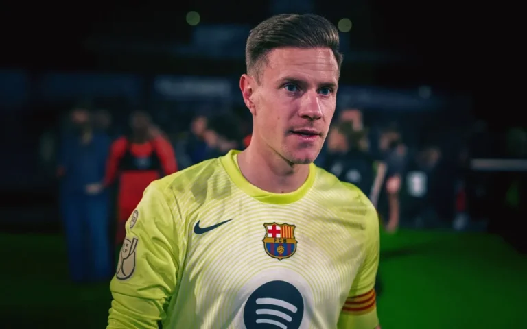 Marc-André ter Stegen mengenakan seragam kiper kuning FC Barcelona dengan sponsor Spotify, berdiri di lapangan sepak bola malam hari