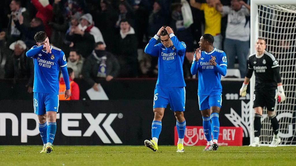 Three Real Madrid players in blue jerseys—likely Arda Güler (6), Dean Huijsen, and another—looking dejected near the goal after Albacete's 3-2 win in Copa del Rey Round of 16 at Estadio Carlos Belmonte, with crowd and Albacete goalkeeper in background.