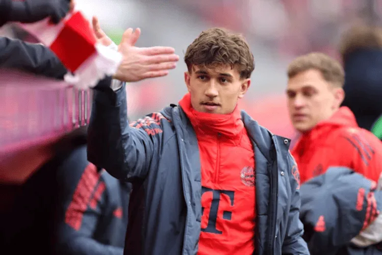 Tom Bischof mengenakan jersey merah Hoffenheim, melambaikan tangan kepada para penonton di pinggir lapangan stadion.